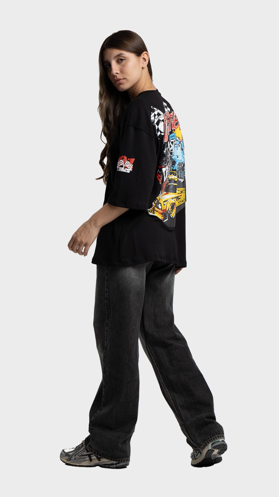 Full body look of a woman wearing a black oversized graphic tee and baggy grey jeans