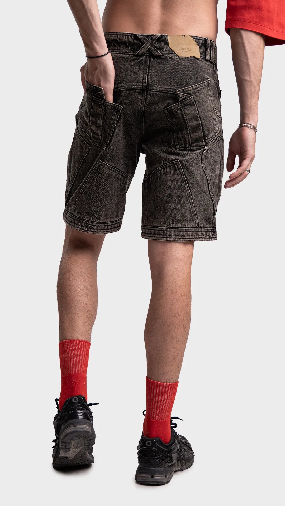 Angled back view of dark grey acid wash jean shorts with hand in pocket.