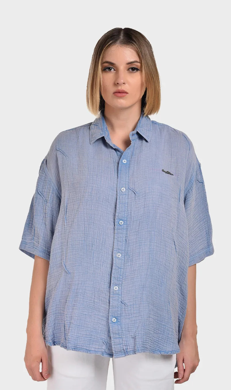 Front view of a women's light blue short-sleeve button-down shirt made from 100% cotton double cloth fabric with a subtle crinkled texture.