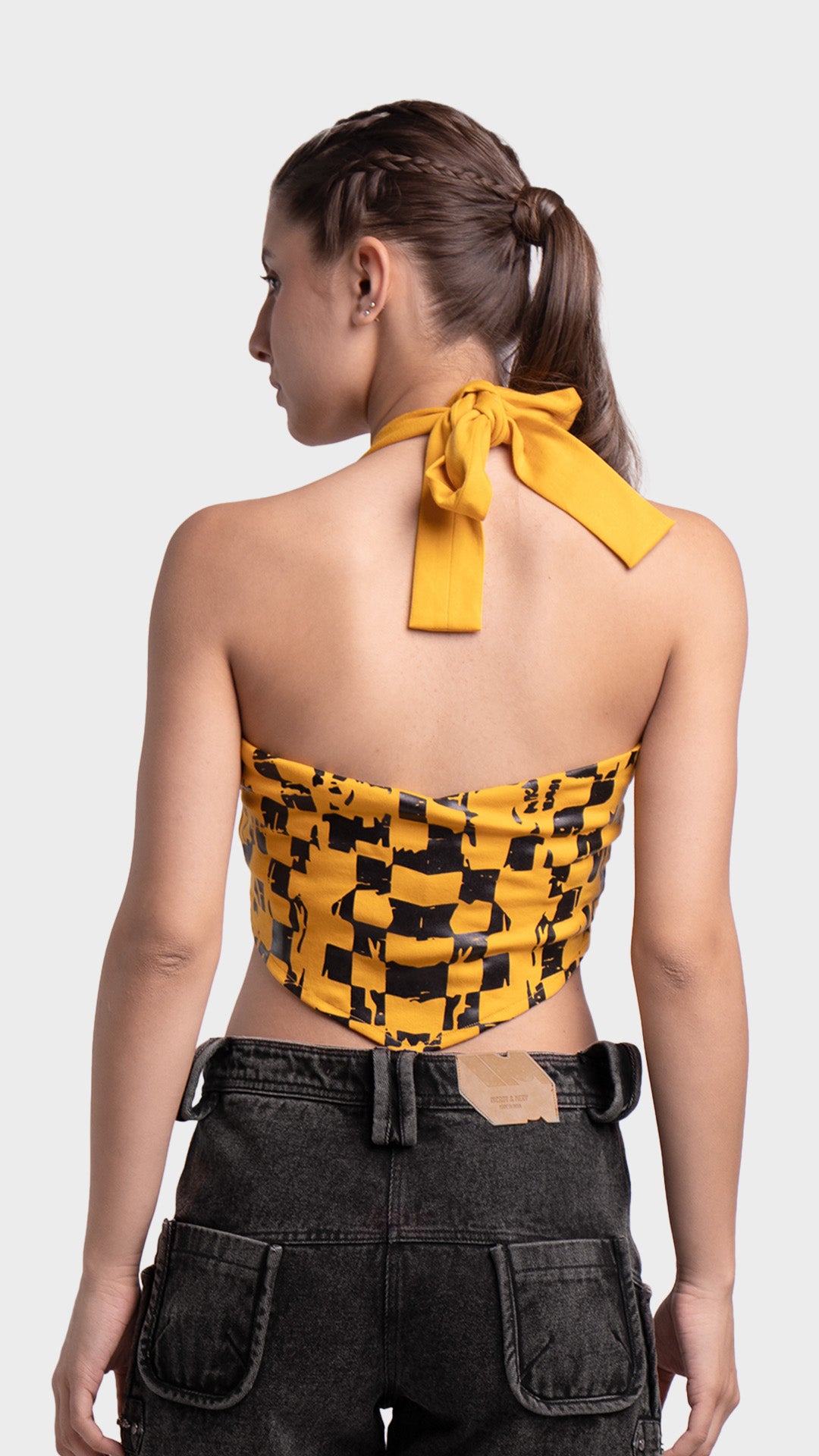 Back view of yellow halter tie-up crop top styled with denim shorts.