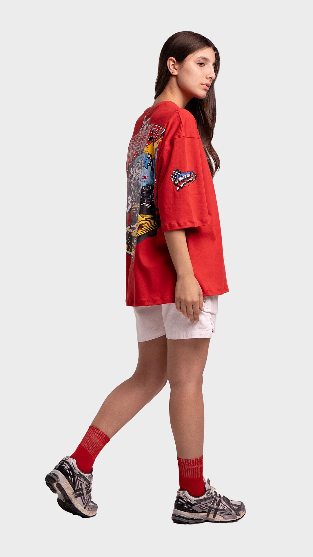 Full body look of a woman wearing a red oversized graphic tee, white shorts, red socks, and sneakers.