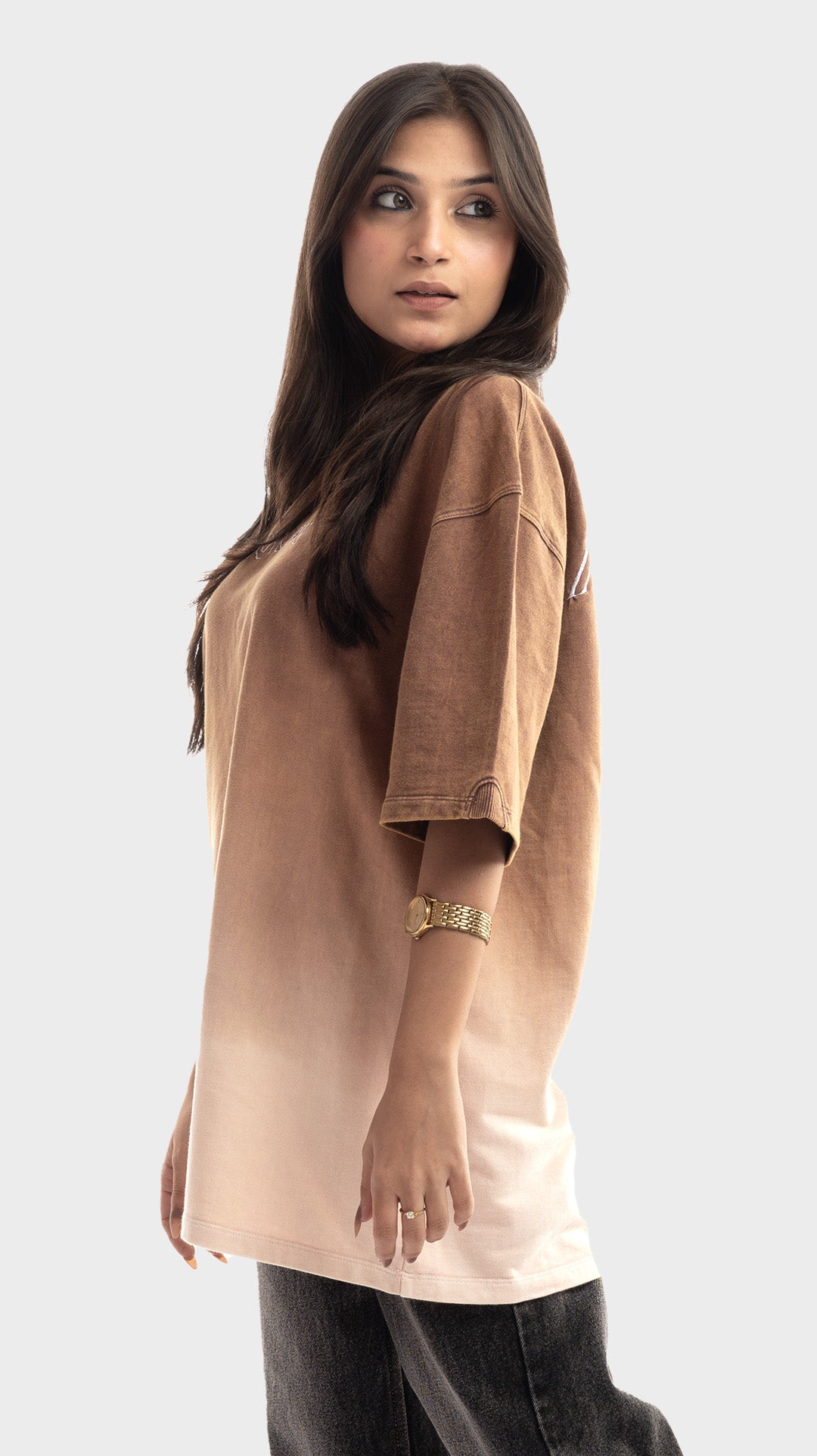 Three-quarter view of a woman wearing a brown to beige gradient oversized tee.