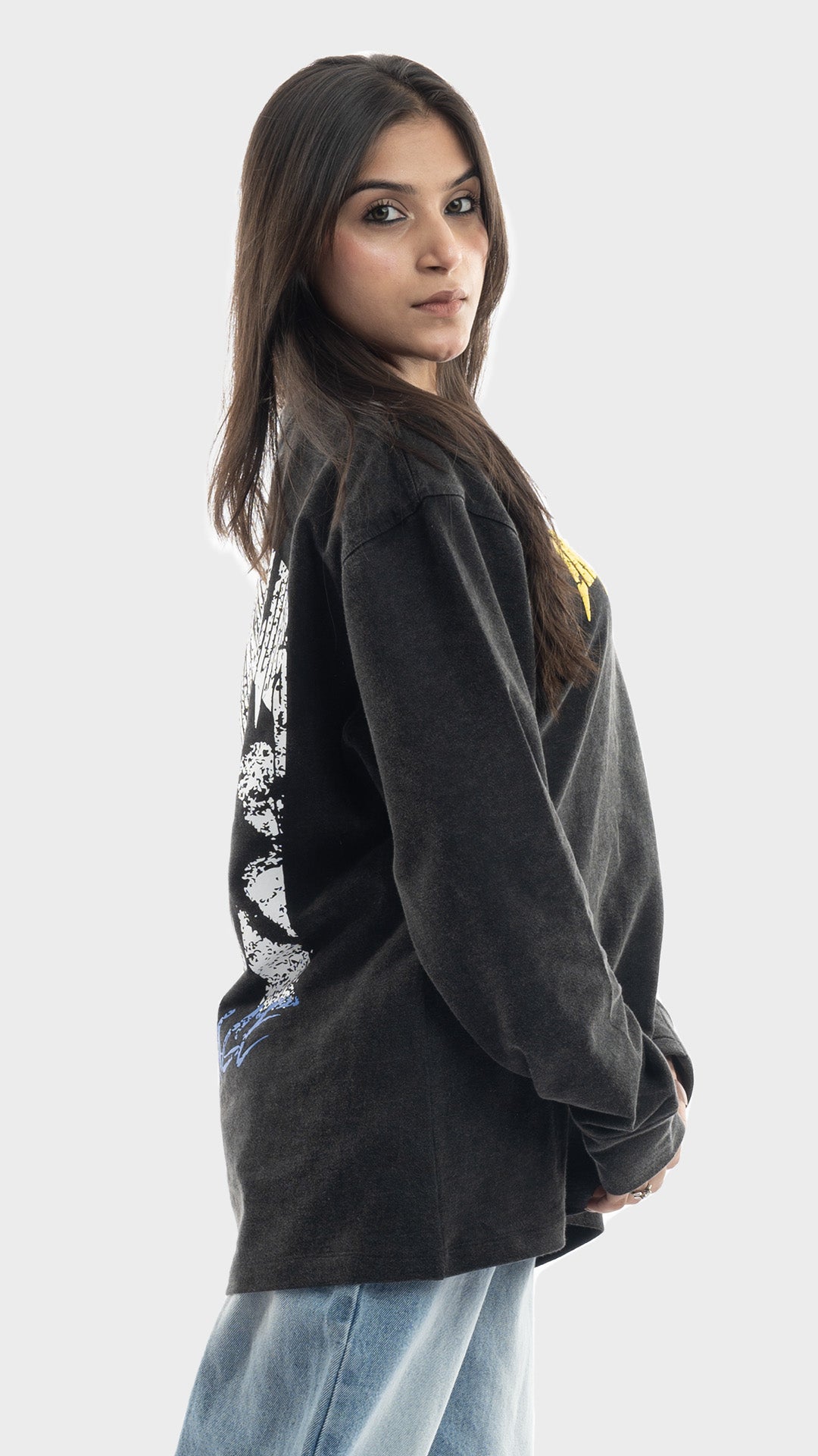 Side view showing the loose fit of a women's charcoal graphic sweatshirt and light blue jeans.
