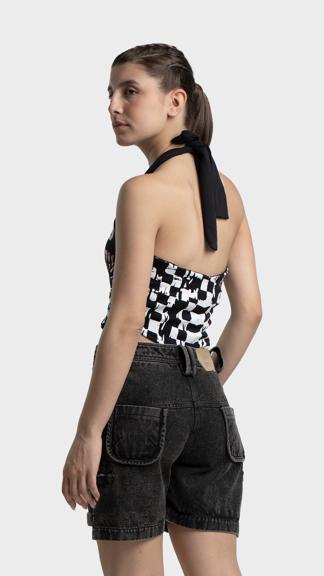 Side view of checkered halter corset top paired with black denim shorts.