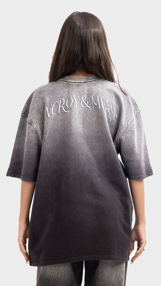 Back view of an oversized acid wash grey ombre t-shirt with white text across shoulders.