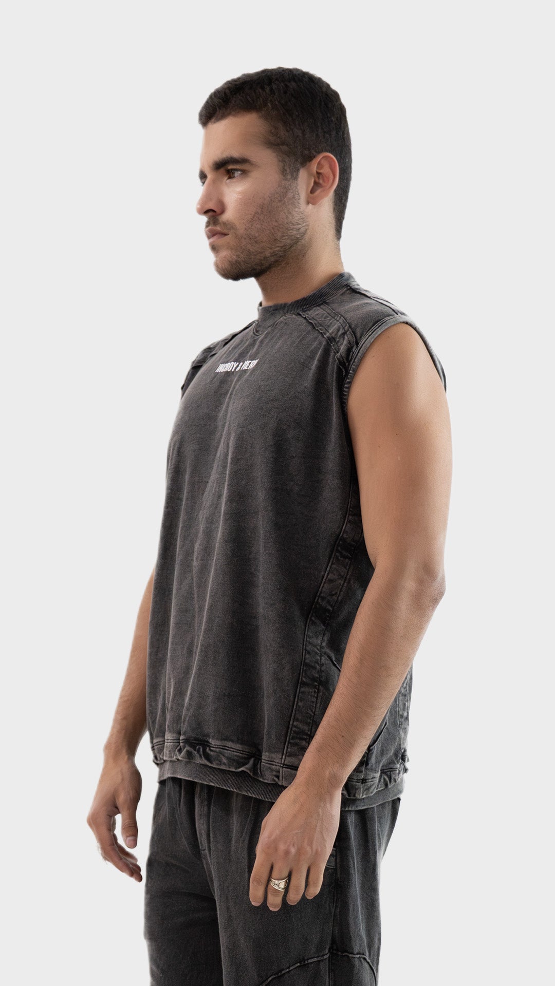 Profile side view of the Incroy and Merv Beyond Tank Top in Charcoal showcasing sleeveless streetwear styling.
