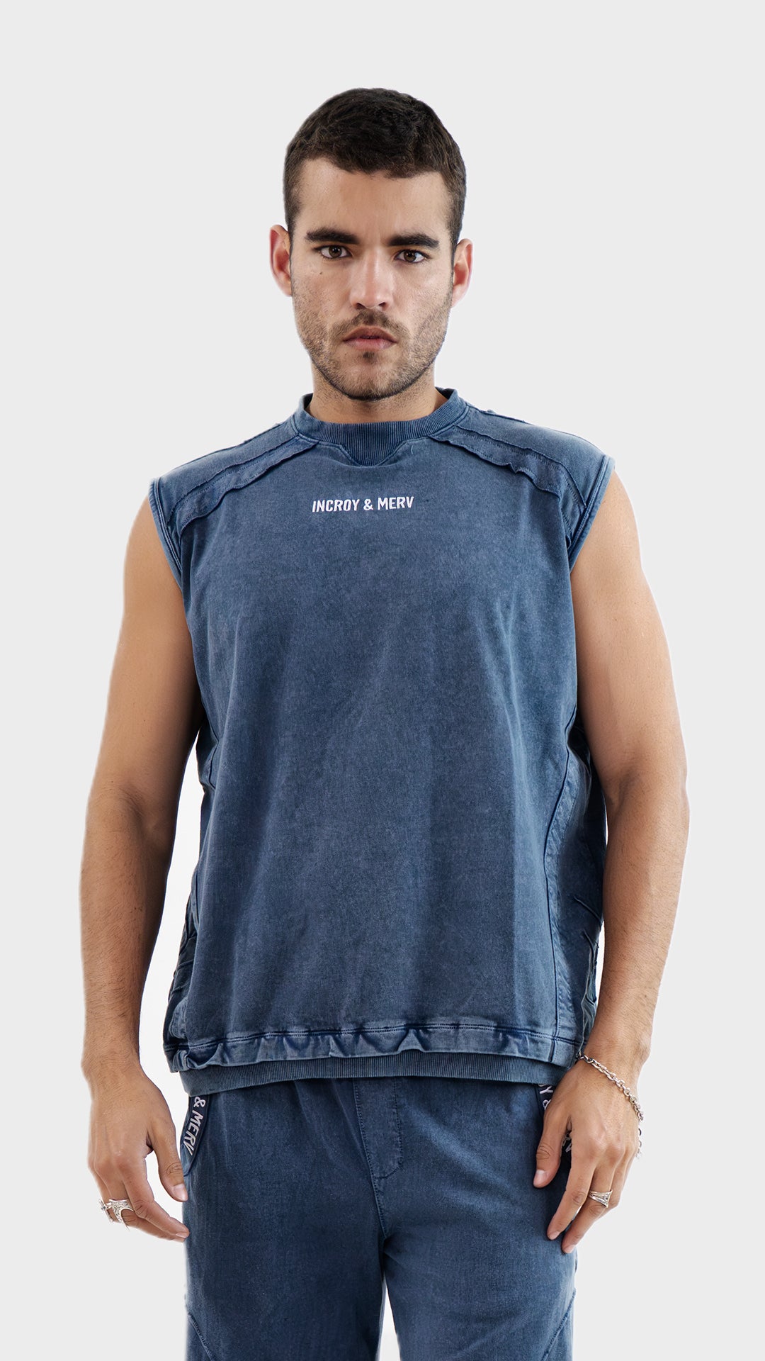 Front view of a man wearing the Incroy and Merv Beyond Tank Top in Dusky Blue made from sinker cotton fabric with chest logo detailing.