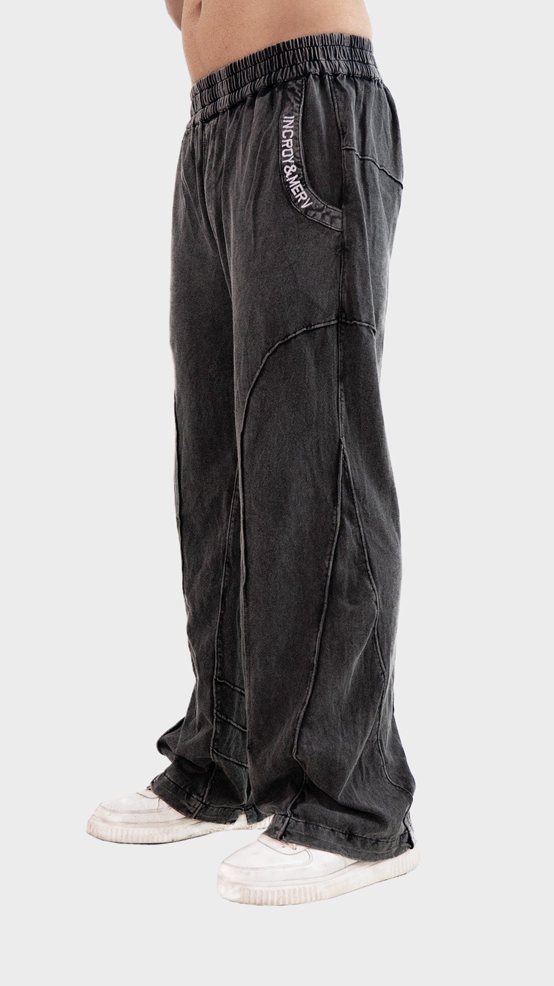 Three-quarter front angle view of Incroy & Merv men's Beyond Trouser in washed charcoal showing side pocket typography embroidery.