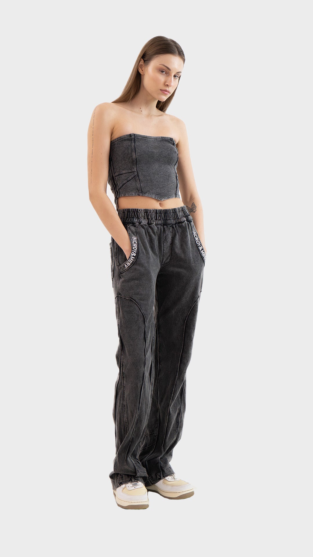 Full length view of model with hands in pockets wearing the Incroy & Merv charcoal Beyond Tube Top and track pants set.