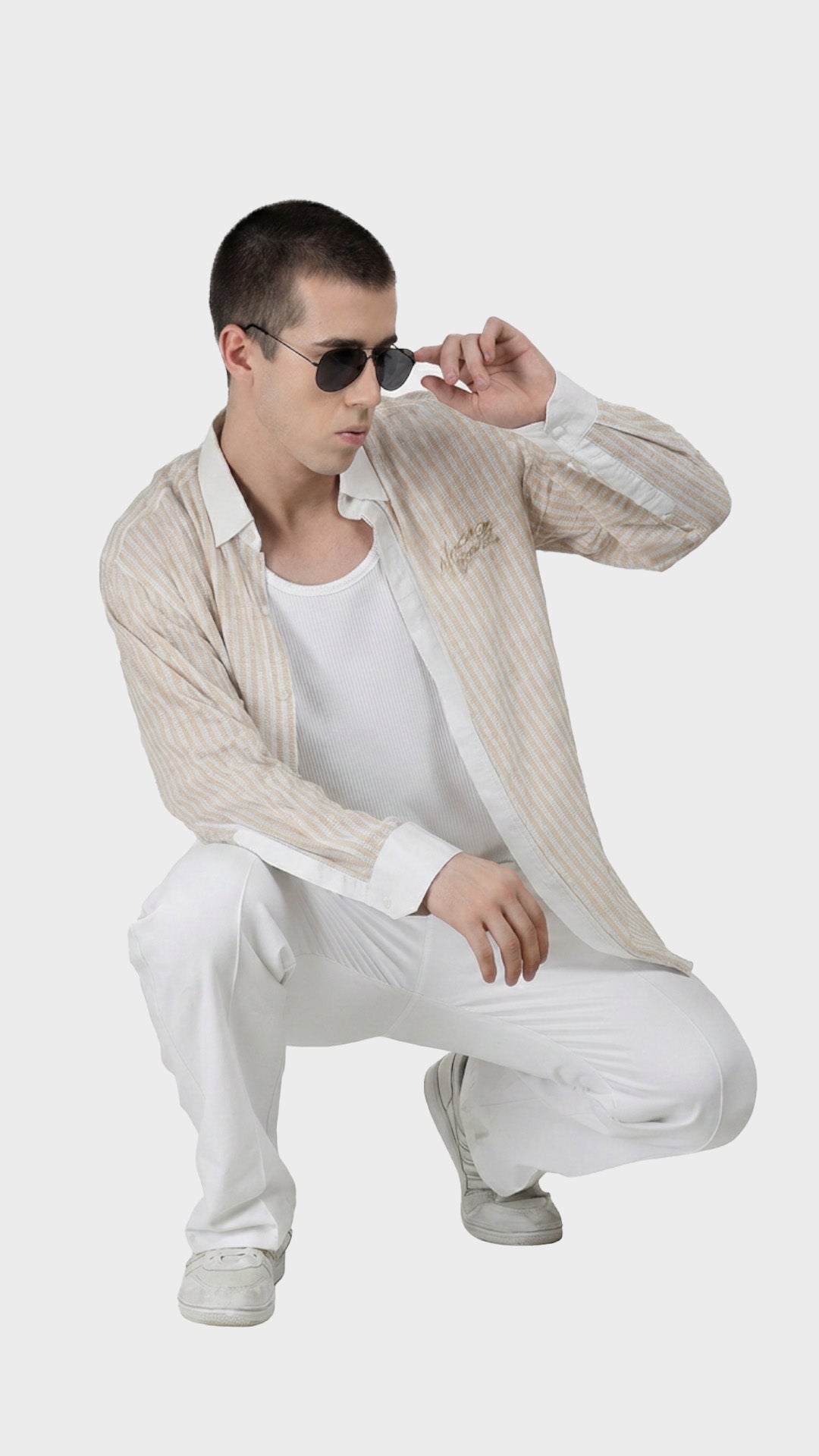 Male model crouching in a beige striped dobby shirt paired with white trousers.