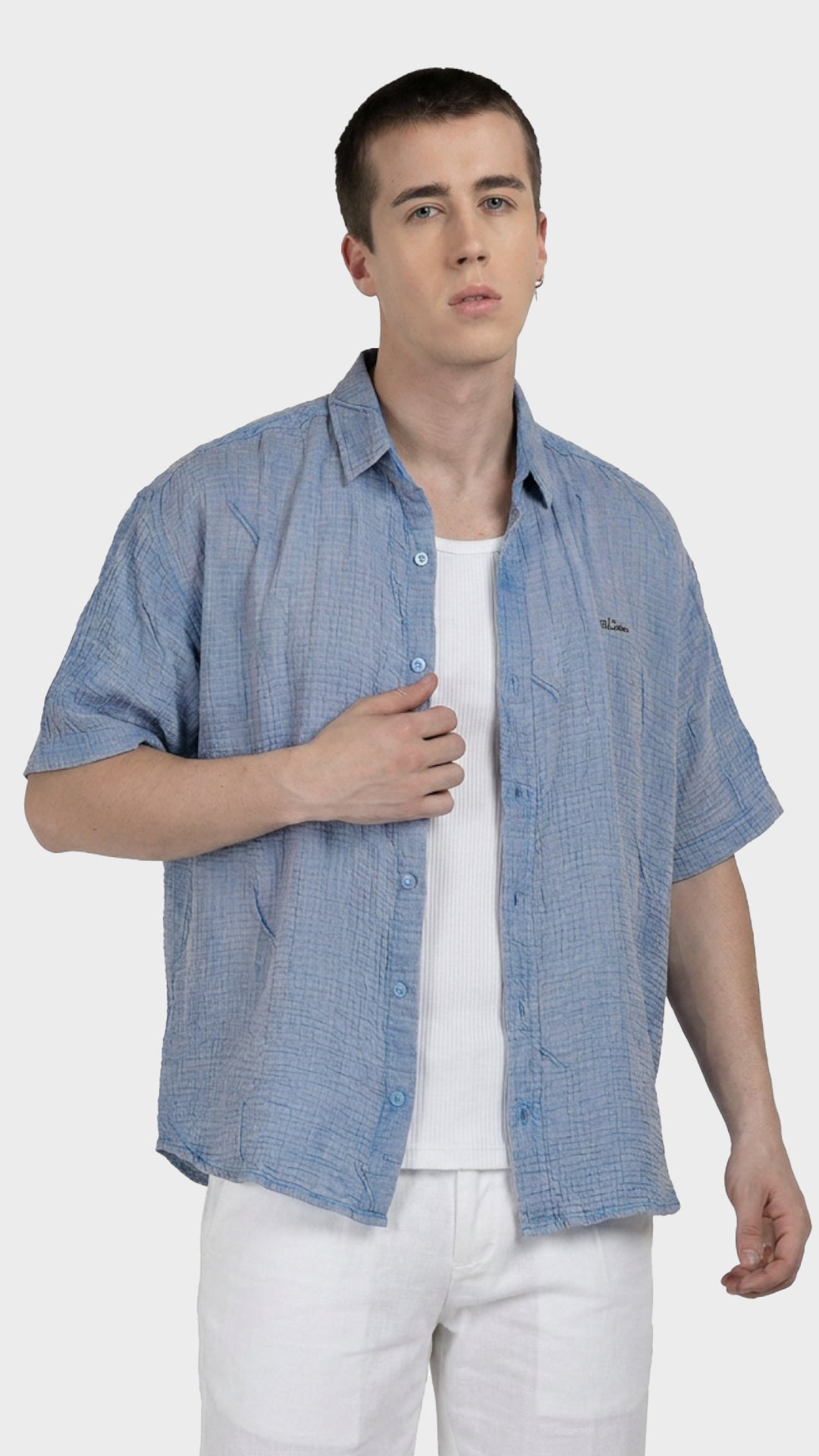Male model wearing an unbuttoned blue 100% cotton double cloth shirt over a white vest.