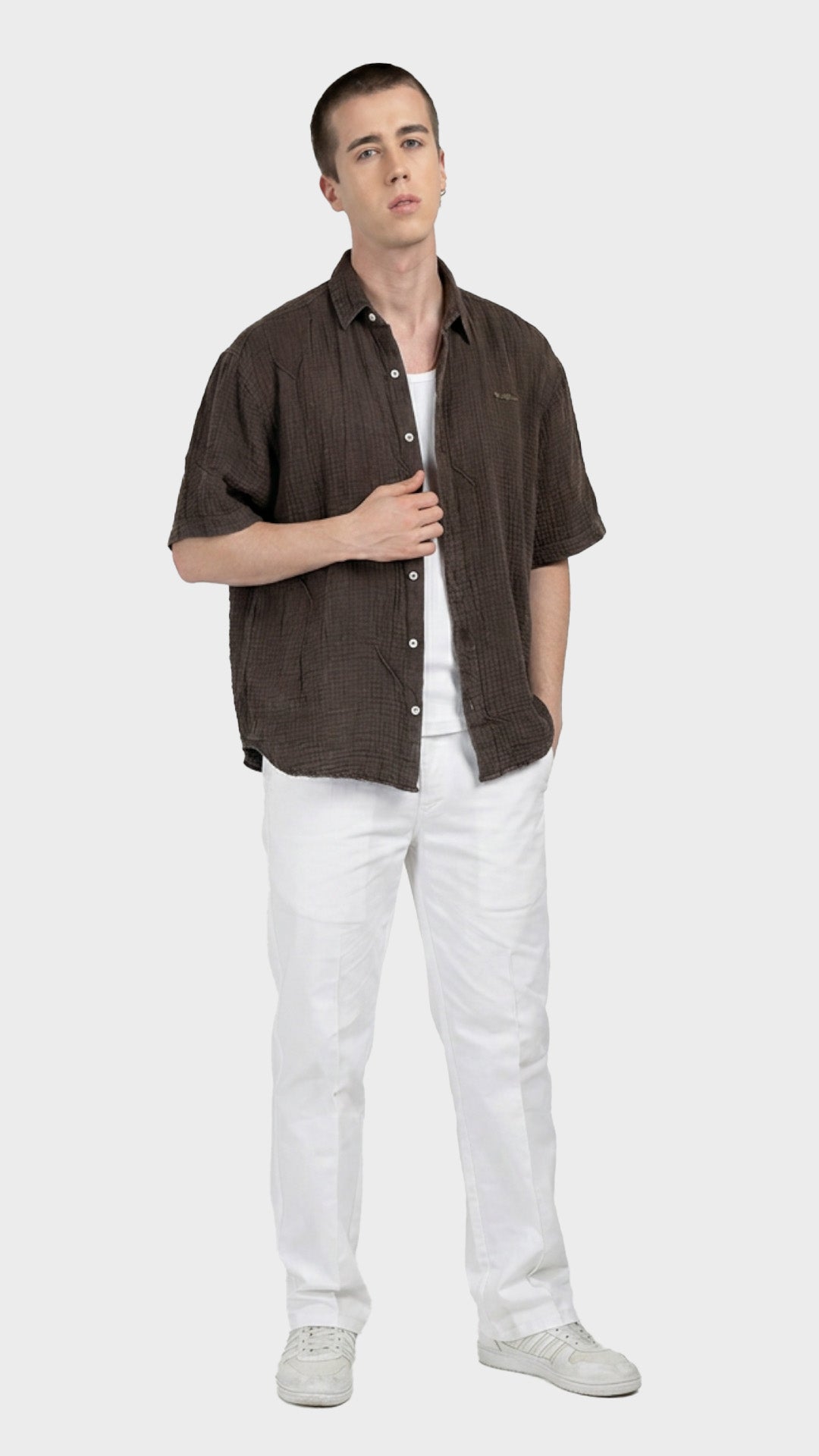 Full-body shot of a male model wearing an unbuttoned dark brown double cloth shirt with white pant.