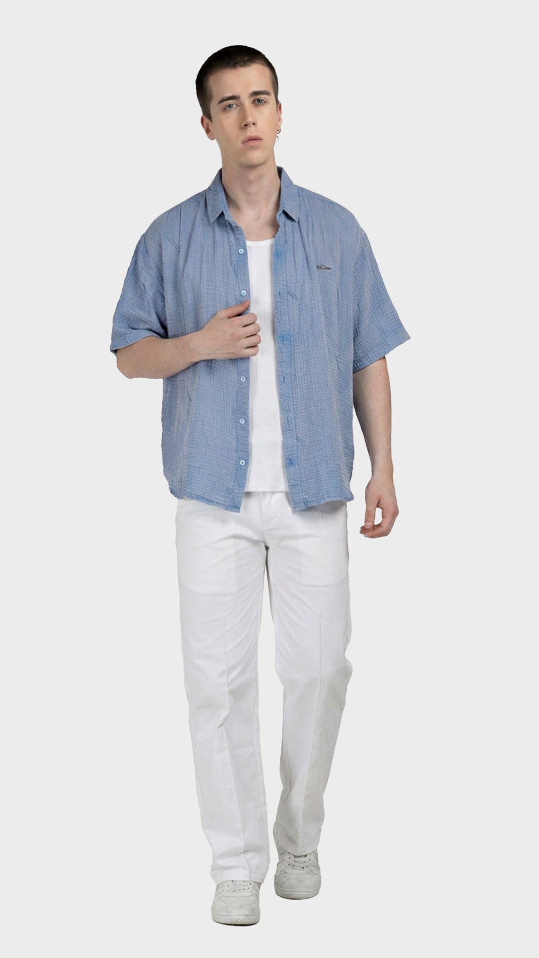 Full-body shot of a male model in a light blue cotton double cloth shirt and white pants.