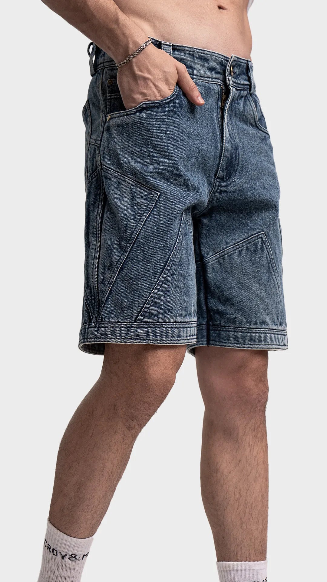 Side detail view of blue acid wash denim shorts with hand in pocket.
