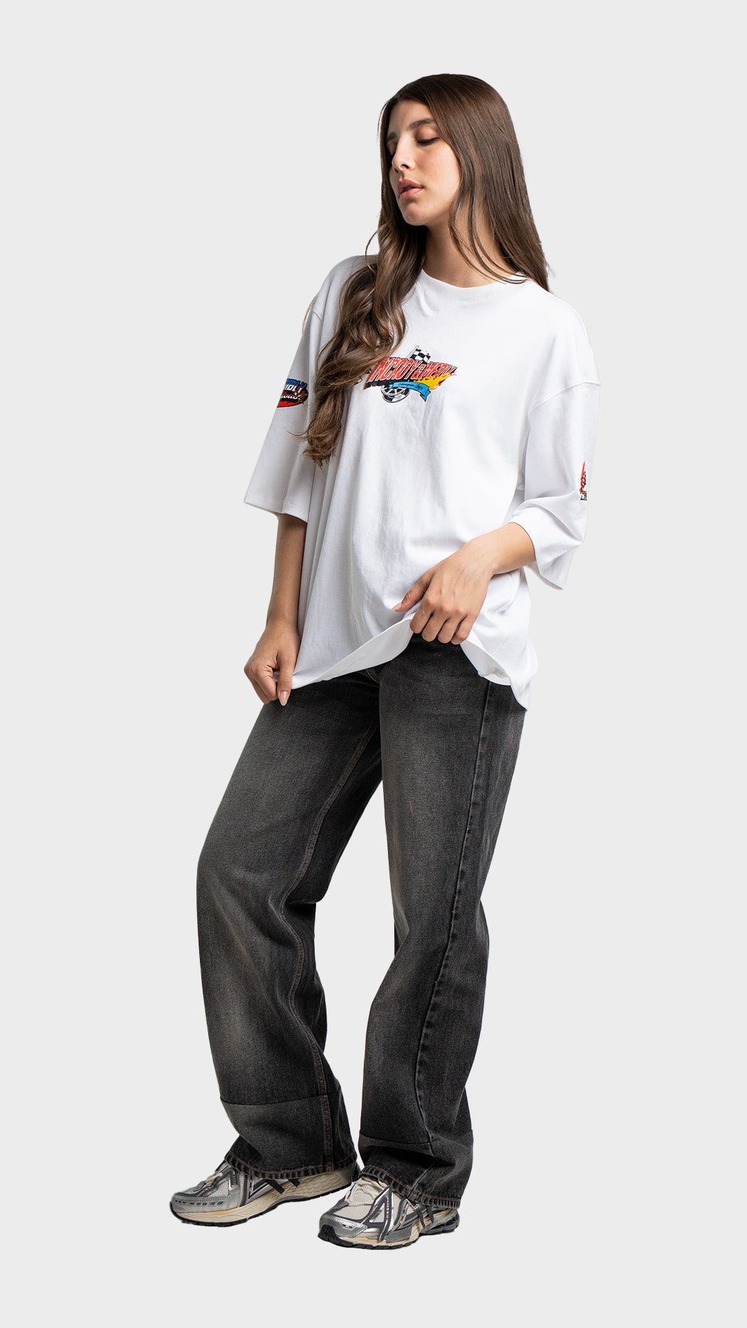 Full body look of a woman wearing a white oversized graphic t-shirt and baggy grey jeans.