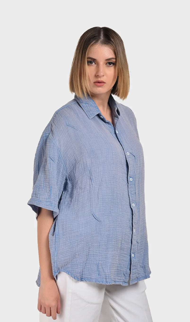 Three-quarter right side profile view highlighting the drop-shoulder short sleeves and soft drape of a women's blue cotton double cloth top.