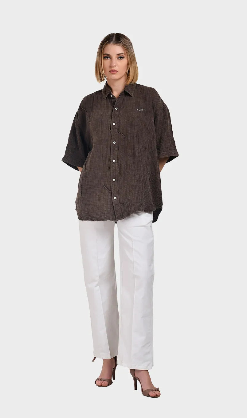 Full-body shot of a model wearing a brown 100% cotton double cloth short-sleeve shirt styled with white high-waisted trousers.