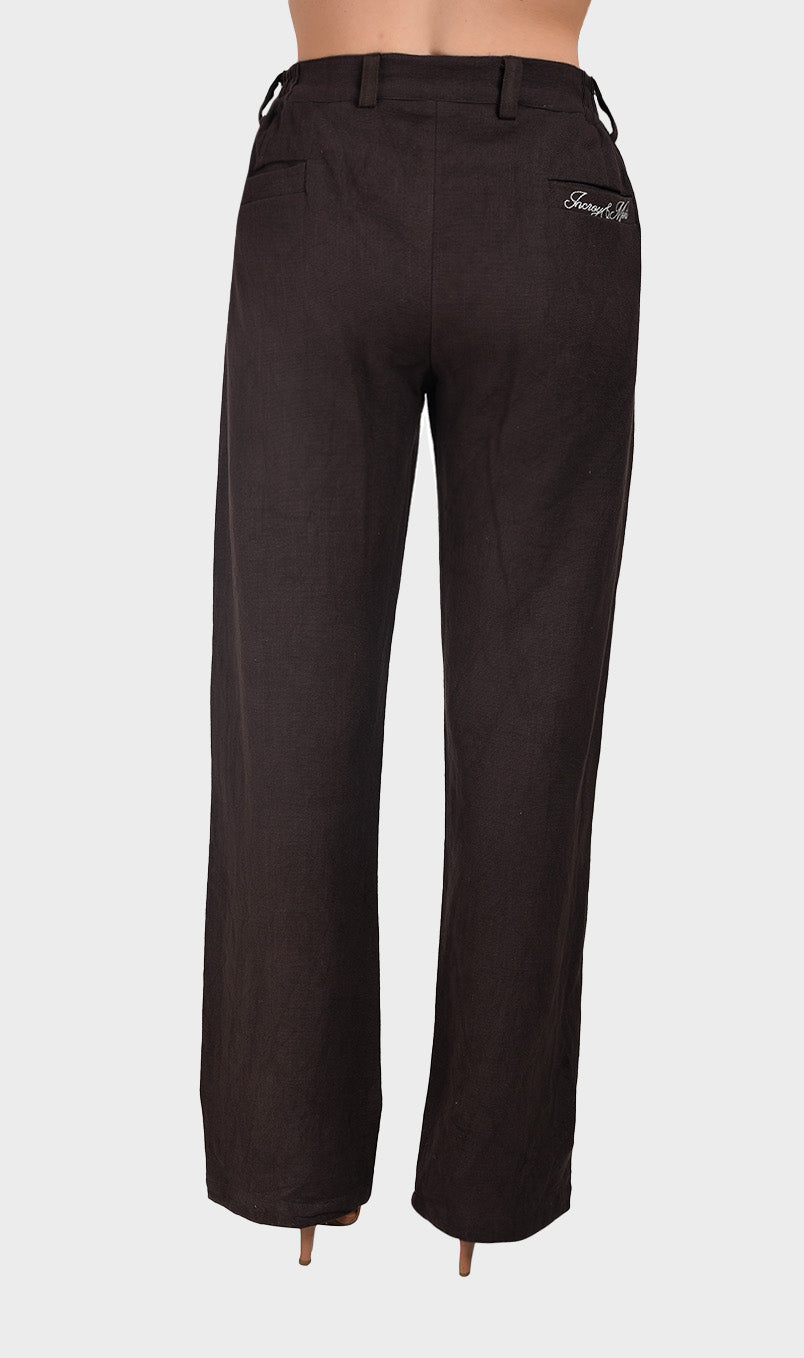 Back view of women's dark brown slub fabric trousers featuring back pockets and subtle embroidery detail.