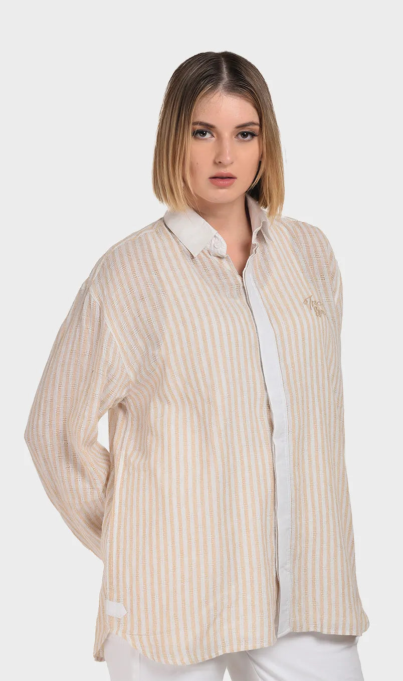 Three-quarter side angle highlighting the woven dobby texture, chest logo embroidery, and relaxed silhouette of a women's beige striped shirt.
