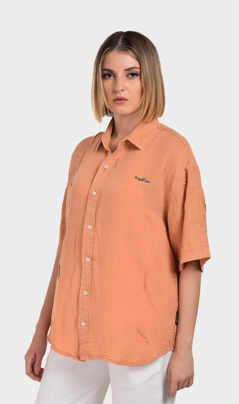 Three-quarter side profile of a model wearing an oversized peach short-sleeve shirt in breathable 100% cotton double cloth.