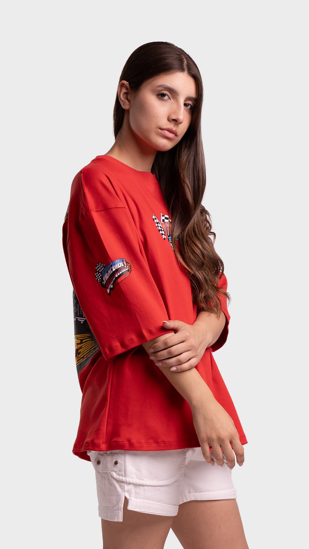 Model posing with arms crossed in an oversized red graphic tee and white shorts