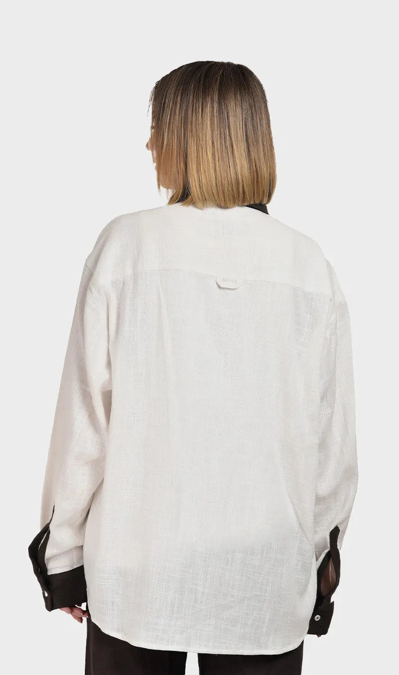 Direct back view showing the subtle slub fabric texture on a women's off-white long-sleeve shirt with brown cuff accents.