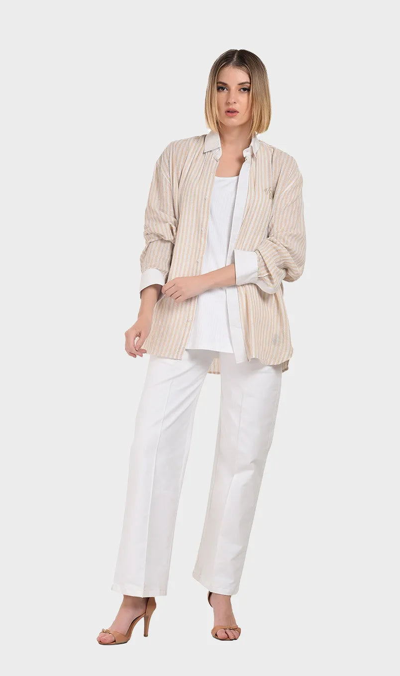 Full-body shot of a model wearing an open beige striped dobby fabric shirt layered over a white top and styled with white wide-leg trousers.
