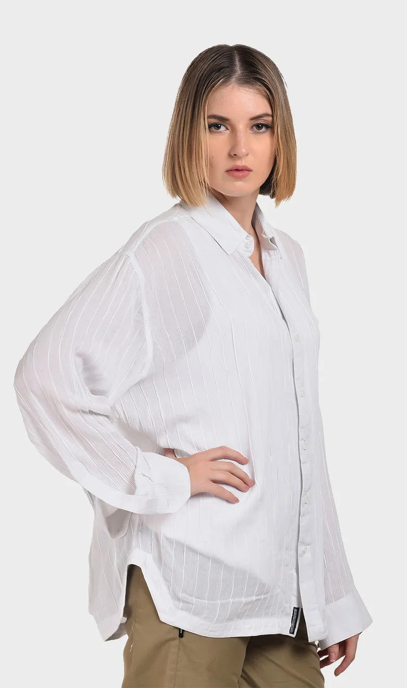 Three-quarter side view of a model posing in an oversized white rayon crepe long-sleeve shirt with cuff details.