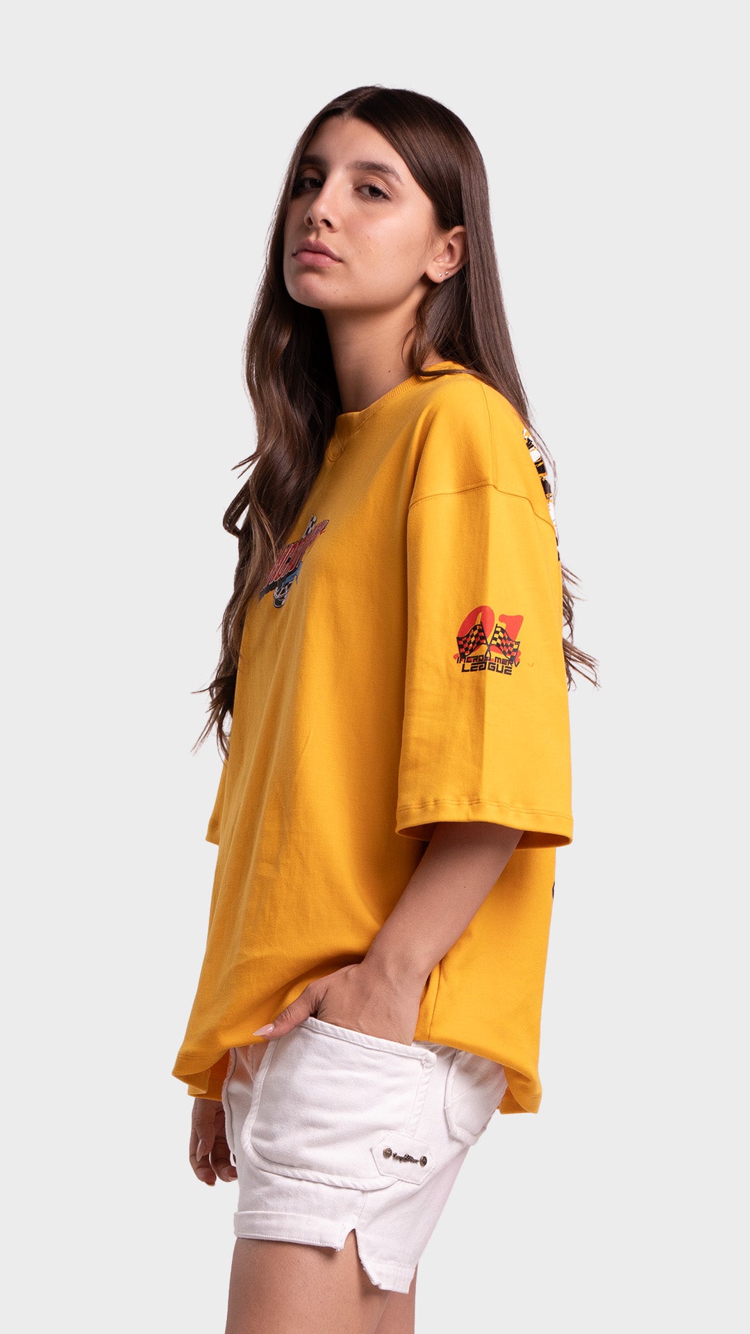 Side profile view of a model posing with her hand in her pocket wearing a yellow oversized racing graphic t-shirt