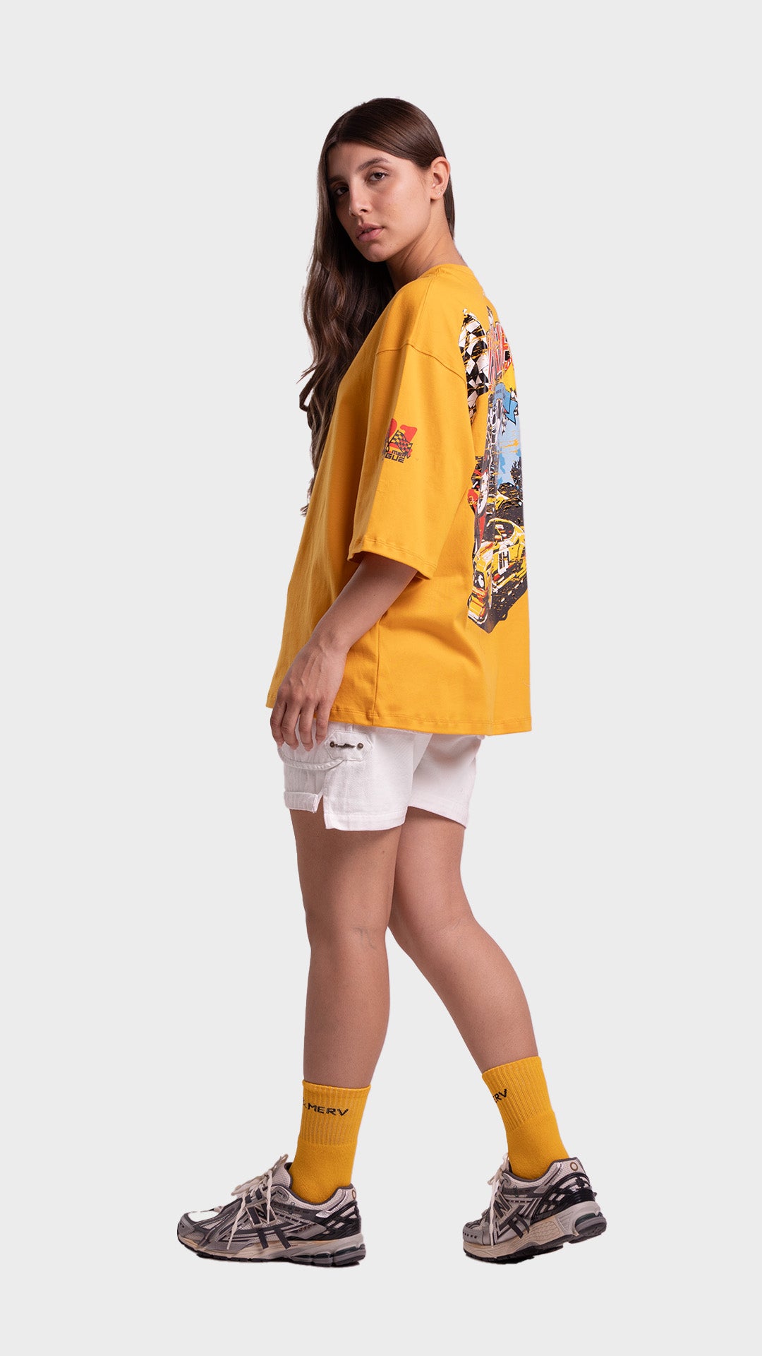 Full body look of a woman wearing a yellow oversized graphic tee, white shorts, yellow socks, and sneakers