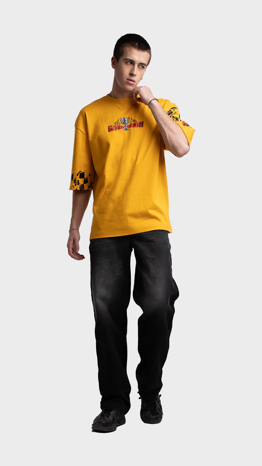 Yellow racing graphic tee outfit for men. Loose fit drop-shoulder streetwear t-shirt styled with baggy black pants.