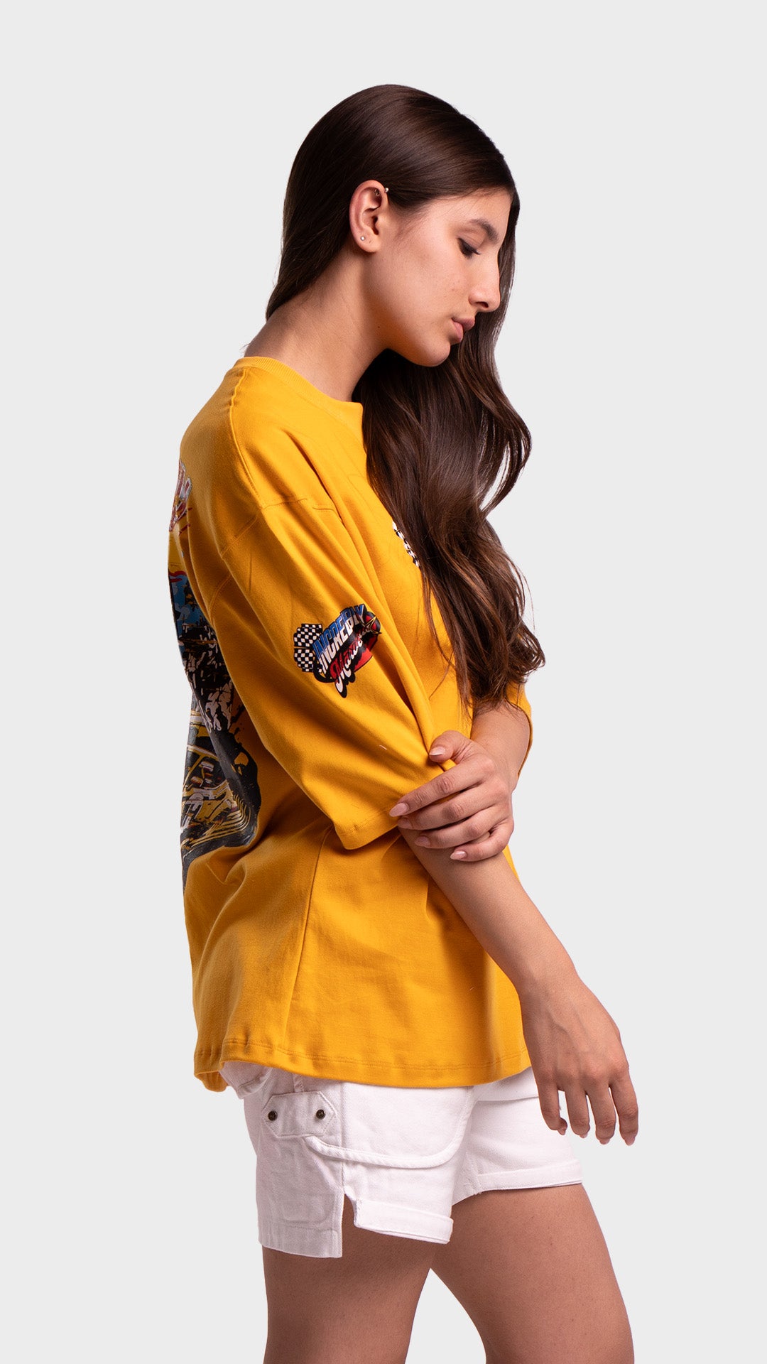 Side profile of a woman with her hand on her arm wearing a yellow loose-fit graphic t-shirt